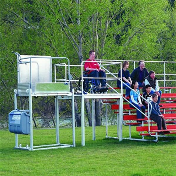 Portable platform lift beside outdoor grandstand seating, a man in a wheelchair on the raised viewing deck