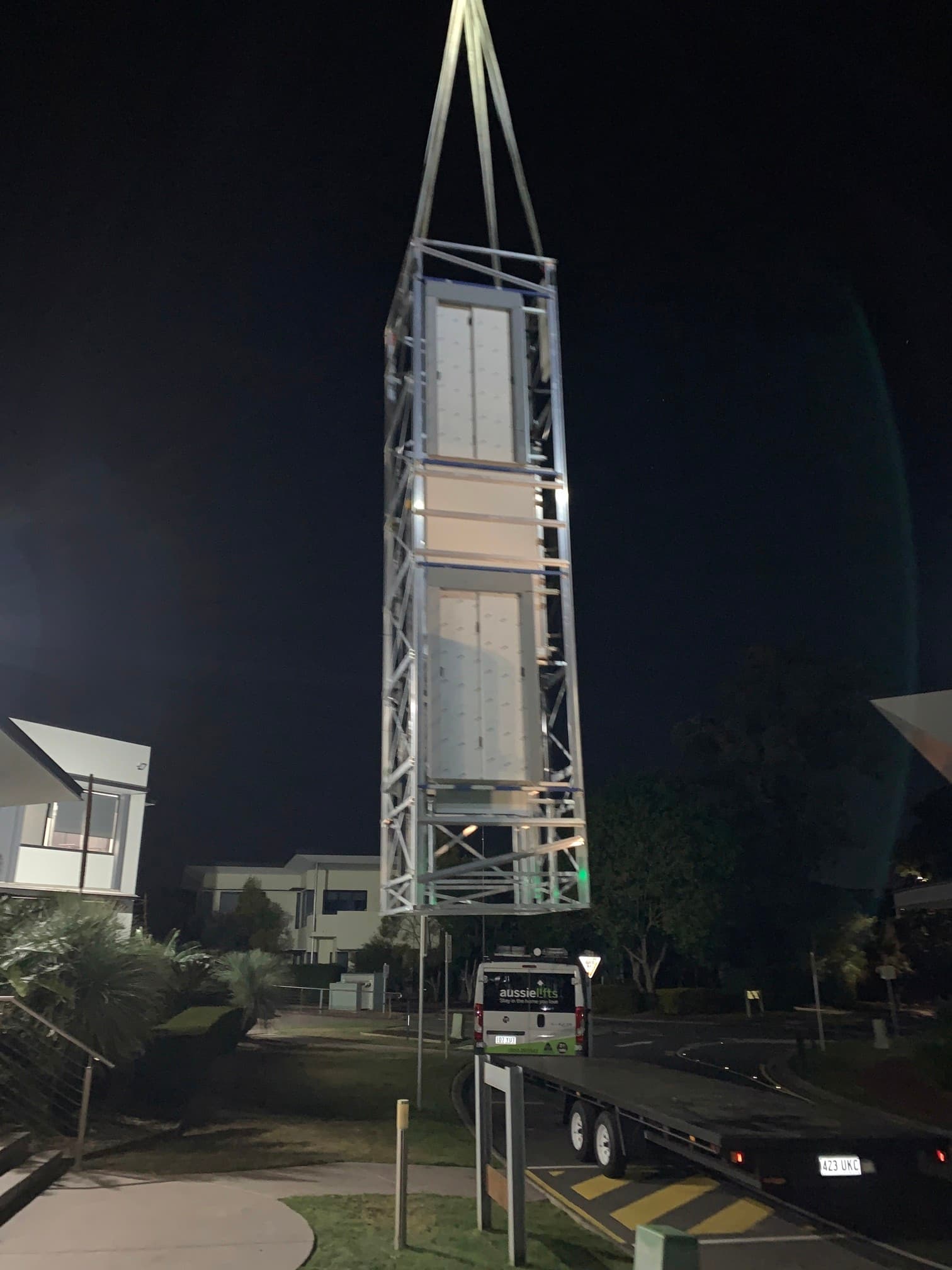 Lift shaft with two landing doors being craned off a truck trailer at night, an Aussie Lifts van parked below
