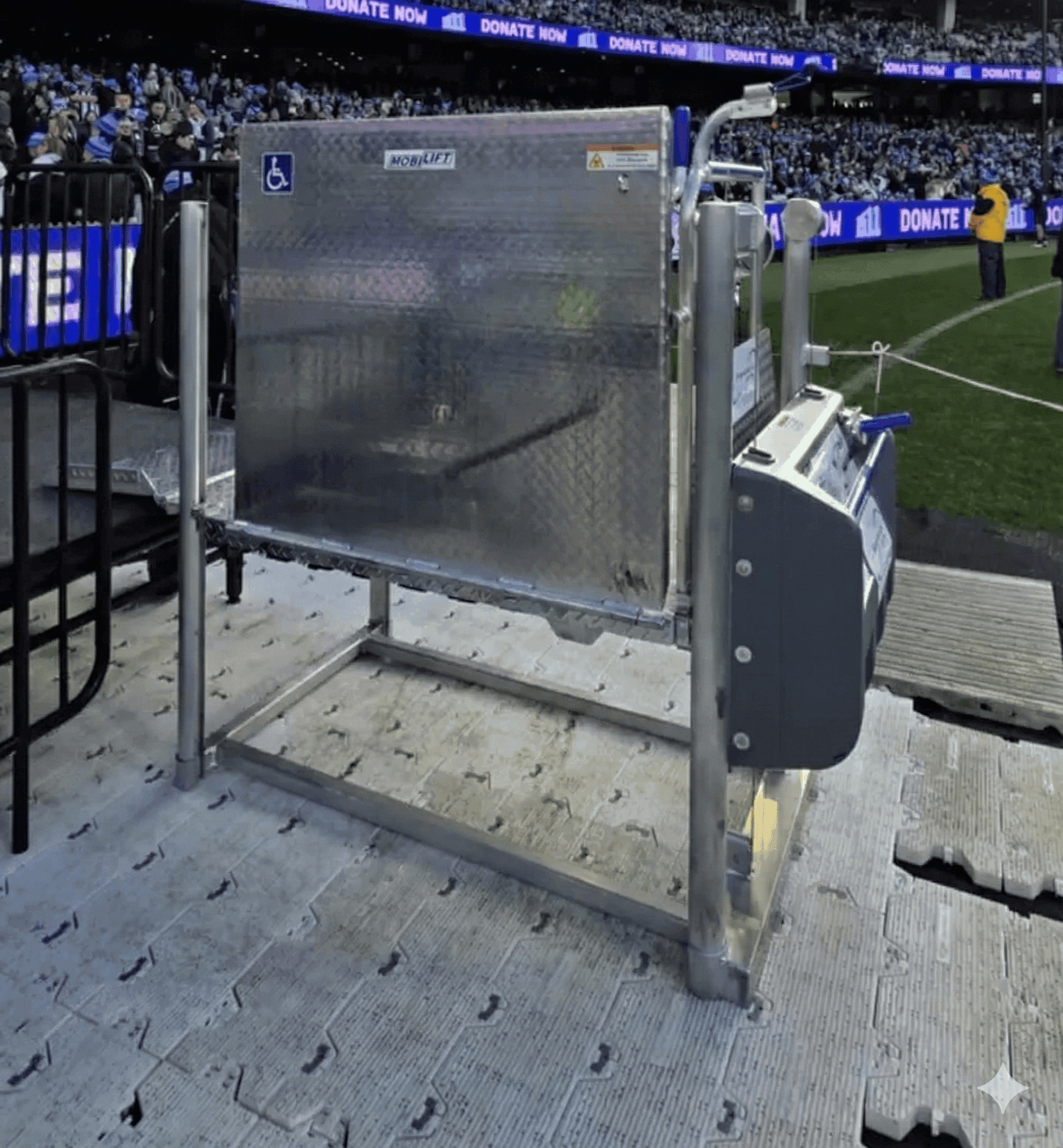 Portable aluminium wheelchair platform lift with a control unit, set up beside the field at a crowded stadium