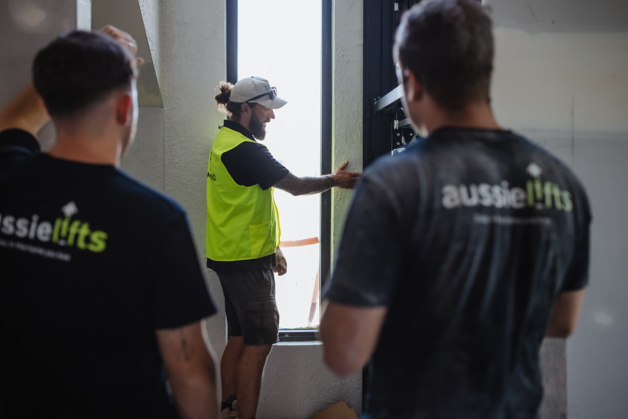 Two Aussie Lifts installers watching a site worker check a lift landing opening