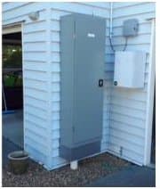 A grey steel machine cabinet mounted on the outside wall of a weatherboard house