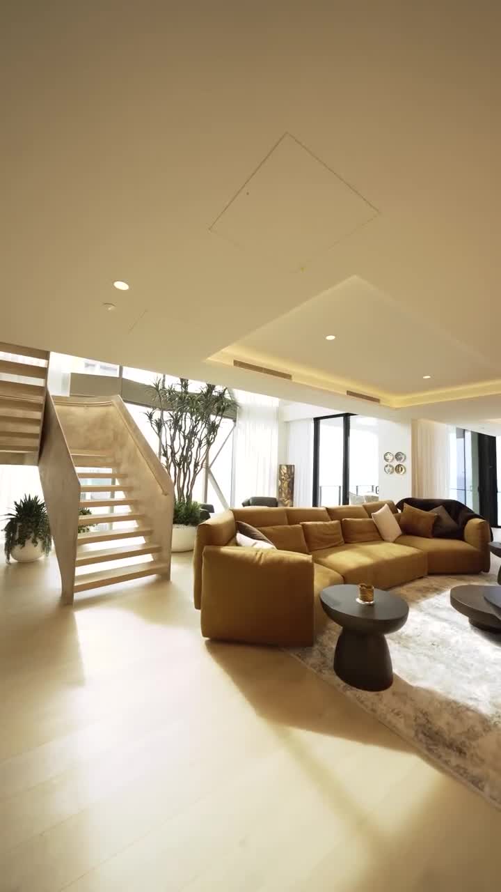 Bright Broadbeach penthouse living room with light timber floors, ochre sofa and a modern timber staircase beside floor-to-ceiling glass