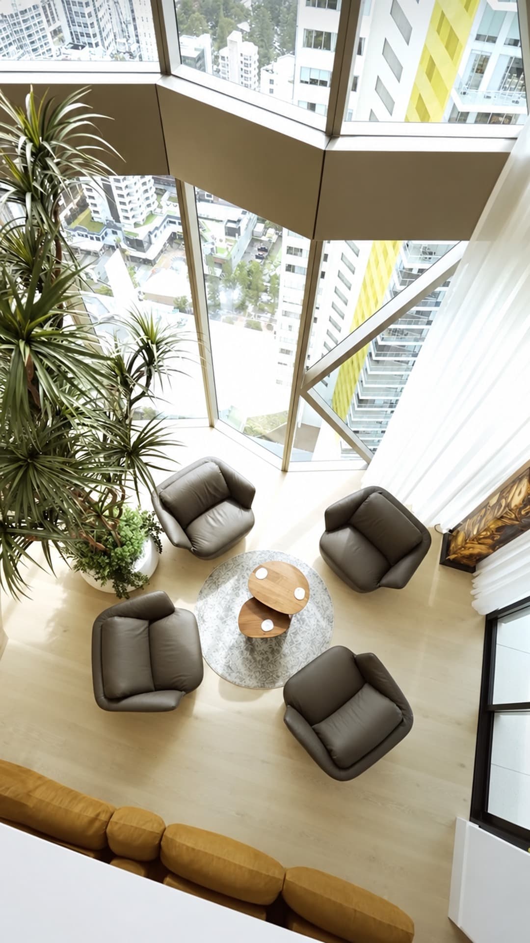 High-angle view of a Broadbeach penthouse living area with charcoal armchairs around a timber coffee table, light timber floors and floor-to-ceiling glass overlooking the Gold Coast