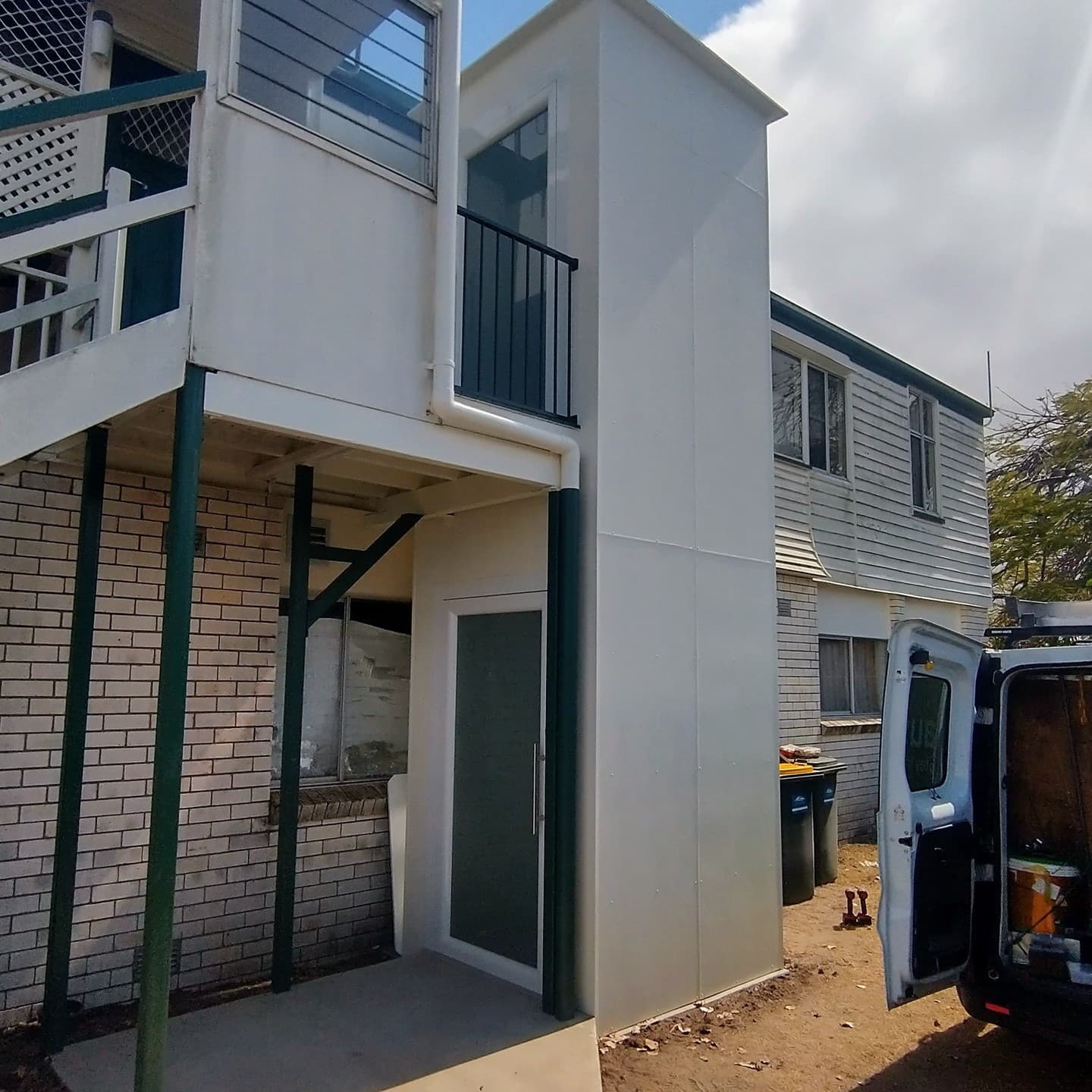A Phoenix home lift in a Bundaberg, Queensland home, finished white external shaft beside a two-storey house with stairs and an Aussie Lifts van