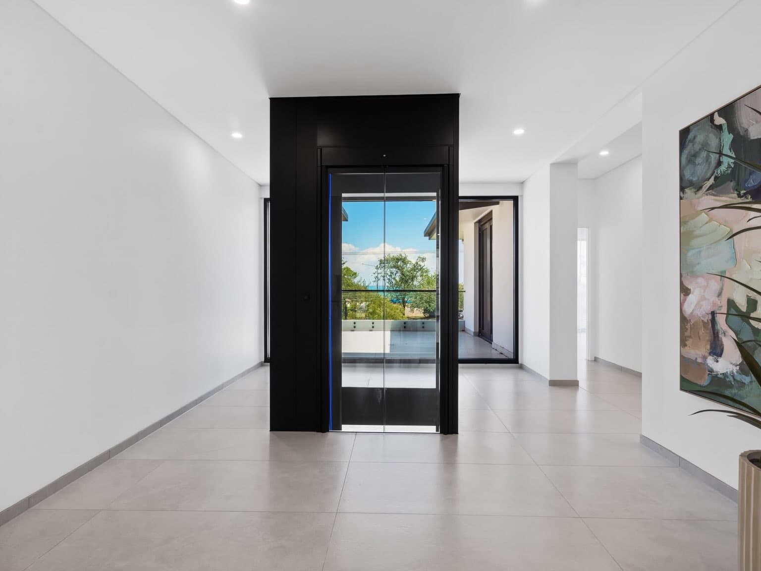 A Swift Pro home lift in a jet black shaft with glass doors and blue RGB lighting on the upper floor of a Fannie Bay, Darwin home, with the water visible through the lift
