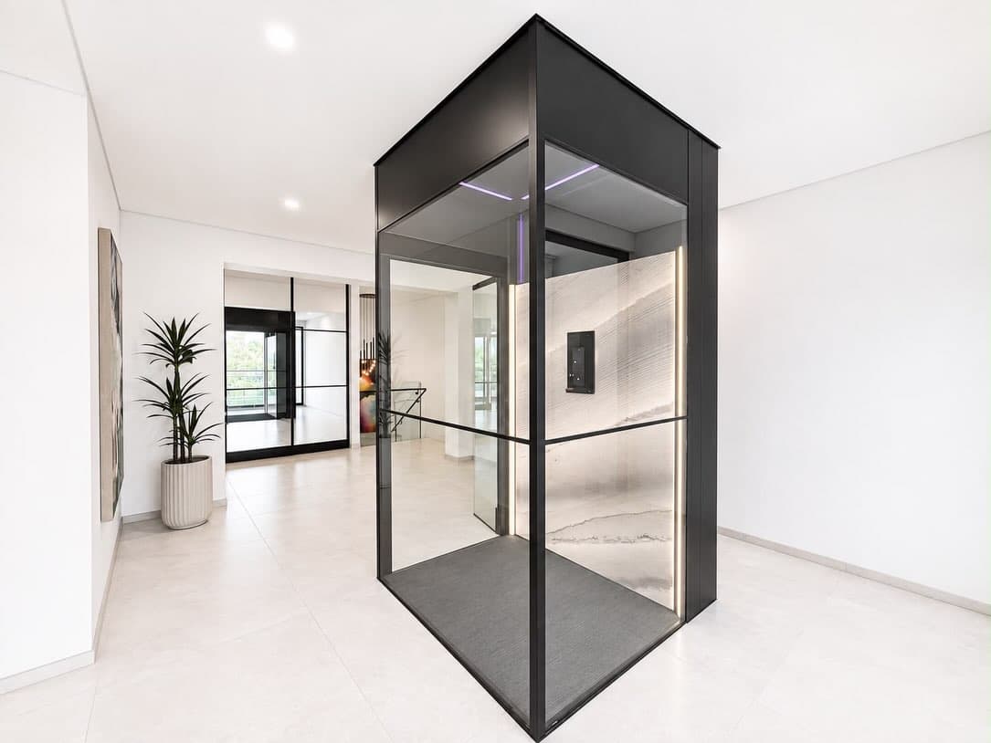 Wide view of the Jet Black Swift Pro shaft in a Fannie Bay hallway: Concrete Artwall, Stitch Black floor, warm LED strips and a touch control panel