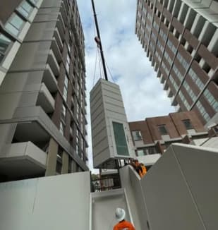A Phoenix lift being craned into a Macquarie Park, Sydney development by ANC Cranes, the modular shaft lowered toward its landing with crew in hard hats and hi-vis below