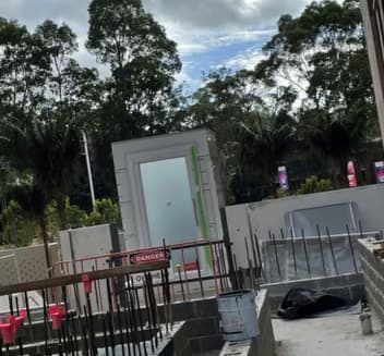 A Phoenix lift shaft with a glass landing door standing in place at a Macquarie Park, Sydney development, with rebar, temporary fencing and a DANGER tag on the site still under construction