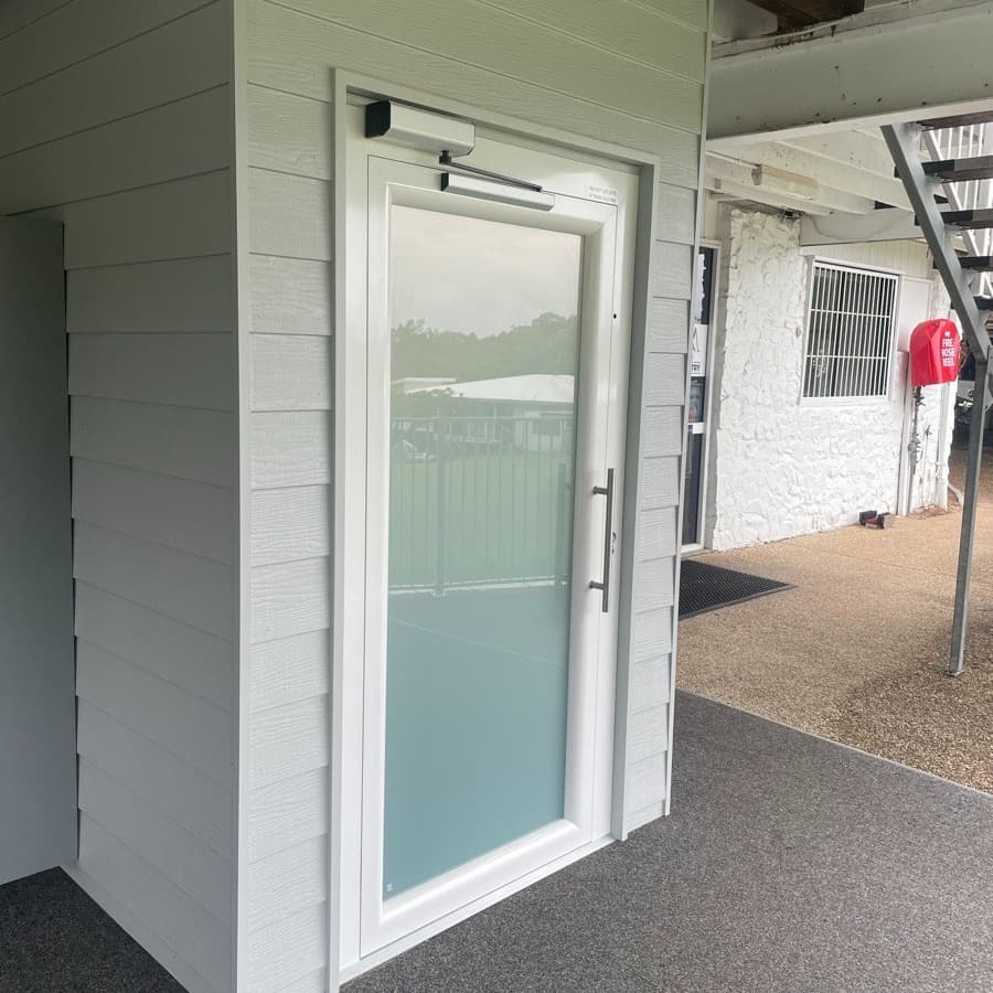 A Phoenix lift at Mt Coolum Golf Course on the Sunshine Coast, exterior landing under the clubhouse deck with grey weatherboard shaft, fire hose cabinet and stairs