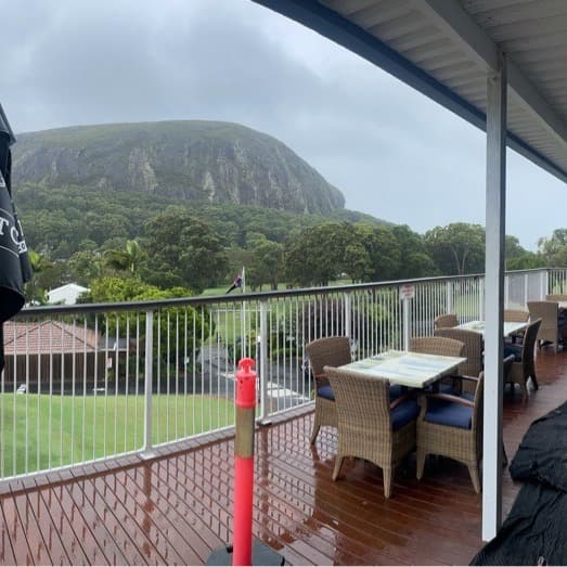 Wet clubhouse deck at Mt Coolum Golf Course looking toward Mt Coolum under an overcast sky. No lift in frame