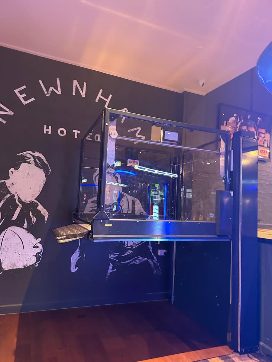 Discovery platform lift raised to the bar level beside the Newnham Hotel mural, under blue bar lighting, Wishart