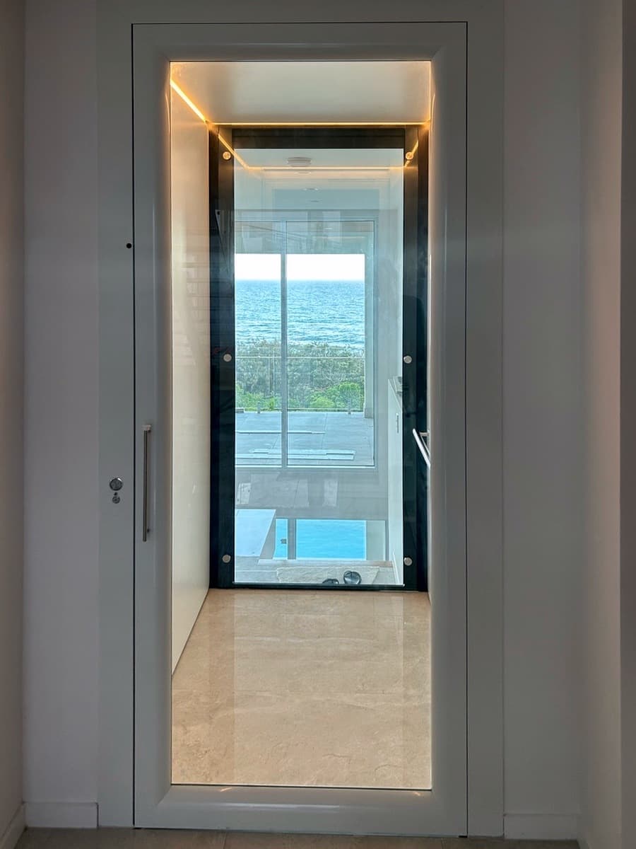 A Phoenix home lift landing door open to a glass cabin with an ocean view in a Sunrise Beach home on the Sunshine Coast