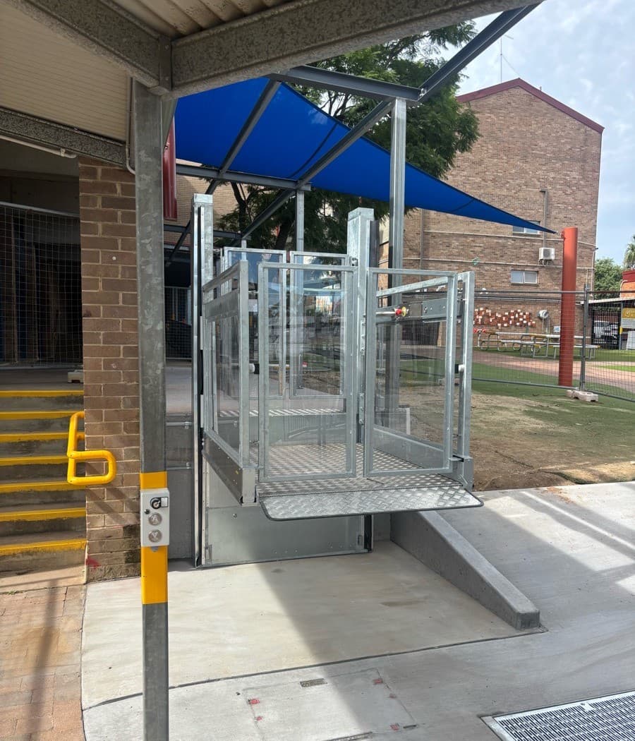Discovery platform lift with glass gates under a blue shade canopy beside the stairs, with a ramp at the lower landing, Westmead school