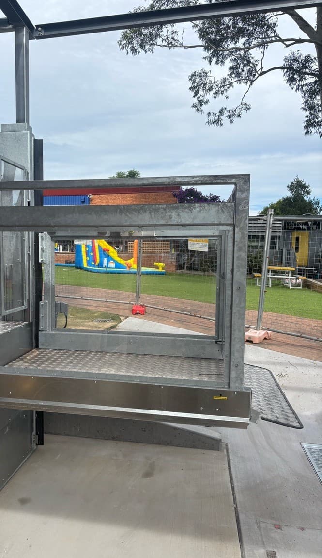 Discovery platform lift at the upper landing with its gate open, the chequer-plate platform looking out to the playground